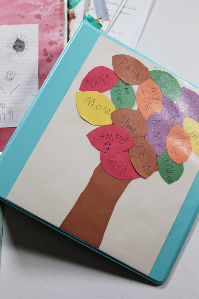 A binder with a child's artwork of a tree inserted in the cover, additional artwork in the background.
