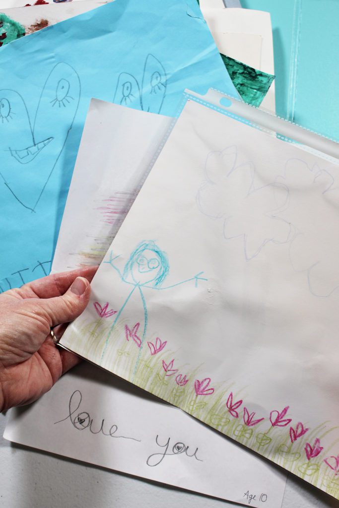 A child's crayon drawing of a person in a field of flowers, other drawings in the background.