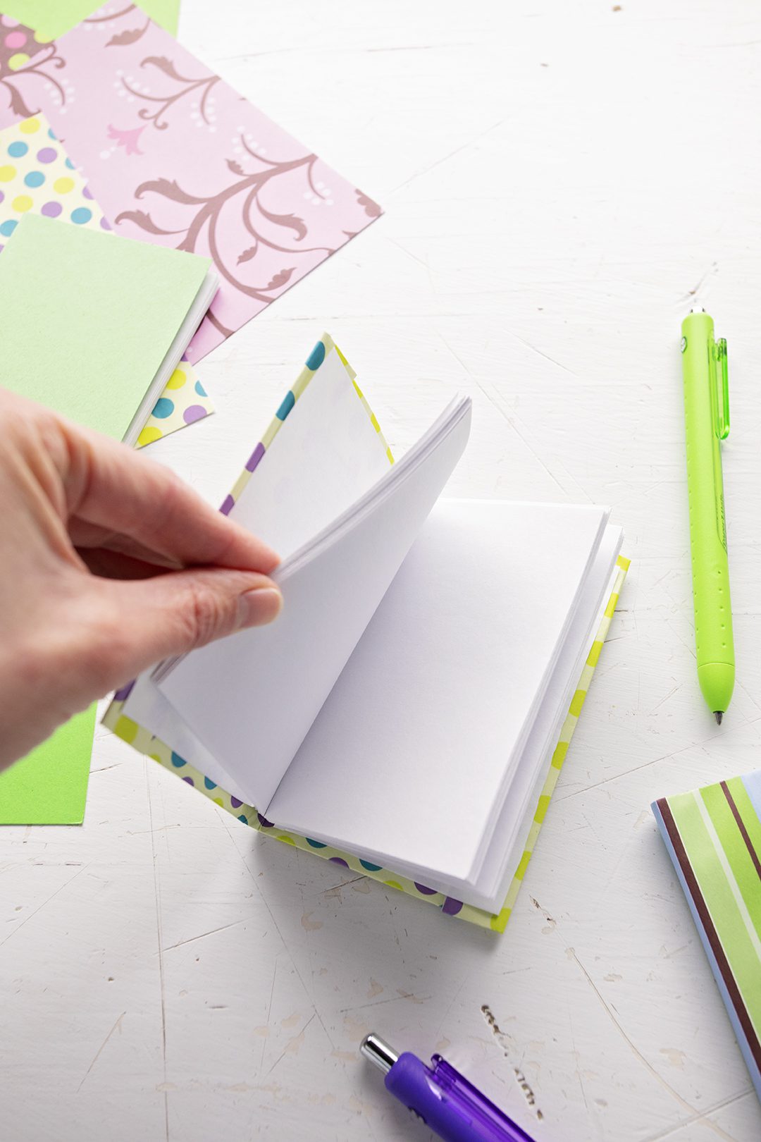 A DIY miniature journal with blank pages, scrapbook paper and pens in the background.