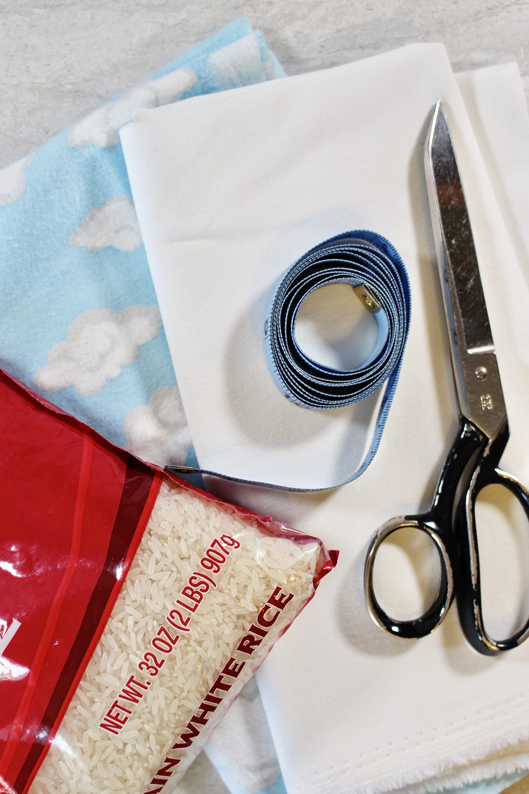 Fleece cloud pattern fabric, a bag of white rice, sewing scissors, and a measurement tape.