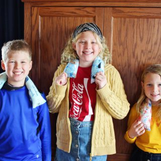 Three children with microwavable rice packs around their shoulders.