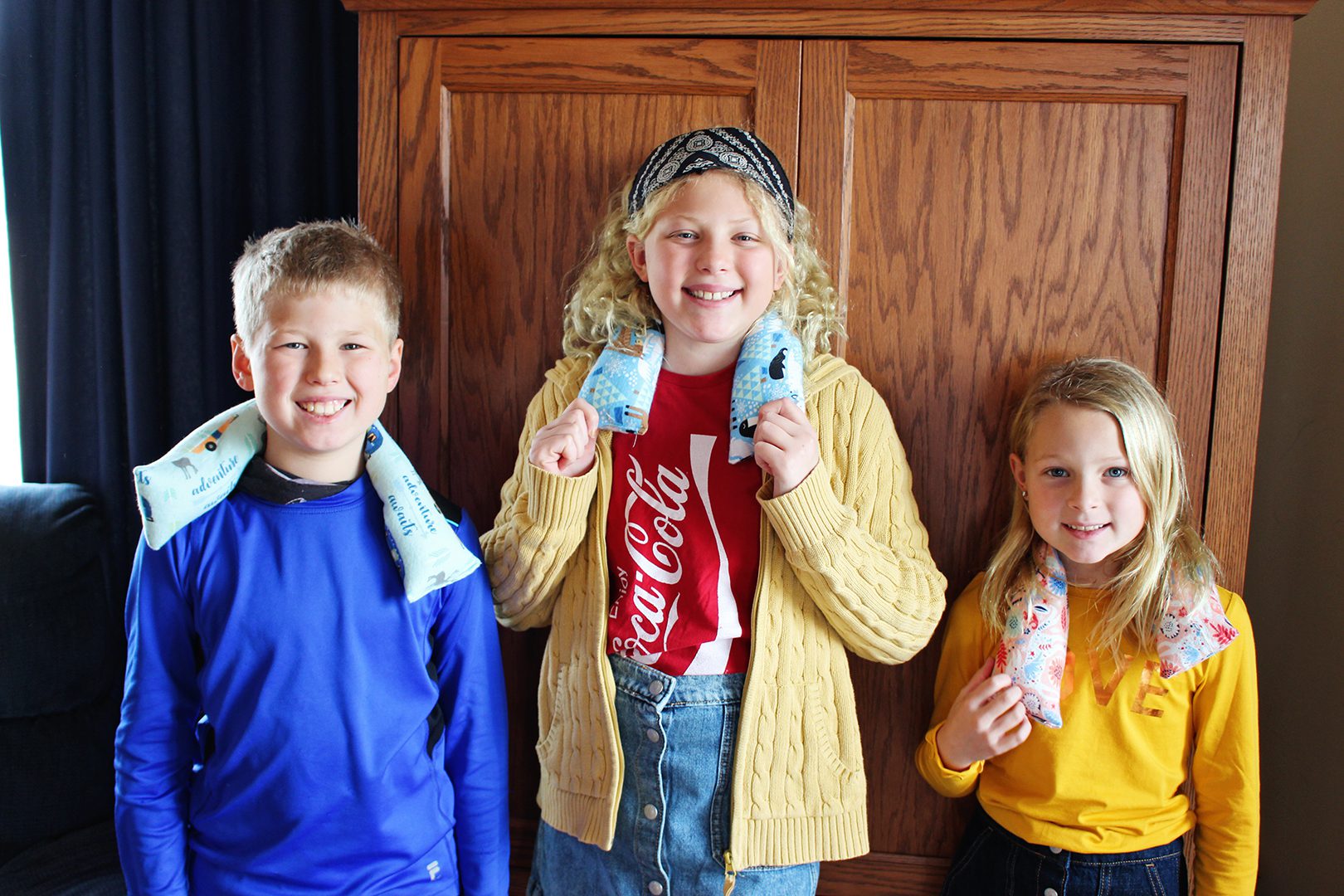 Three children with microwavable rice packs around their shoulders.