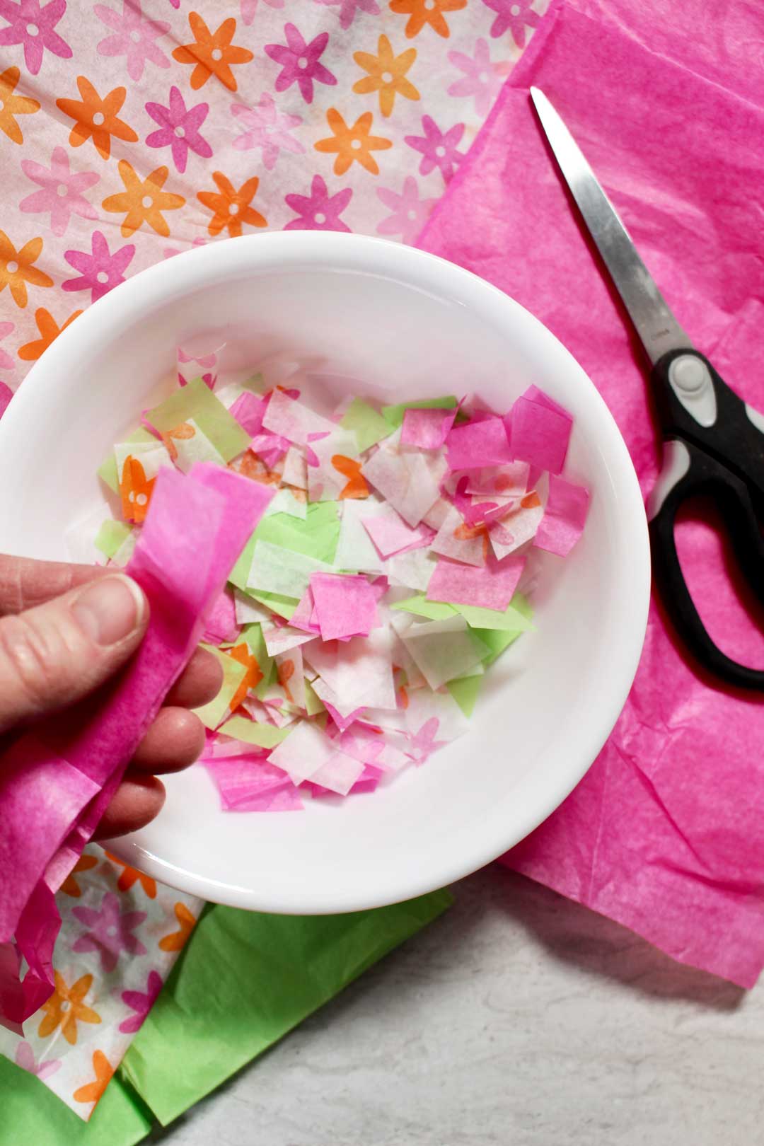 Pink, green, and white tissue paper cut into squares in a bowl.