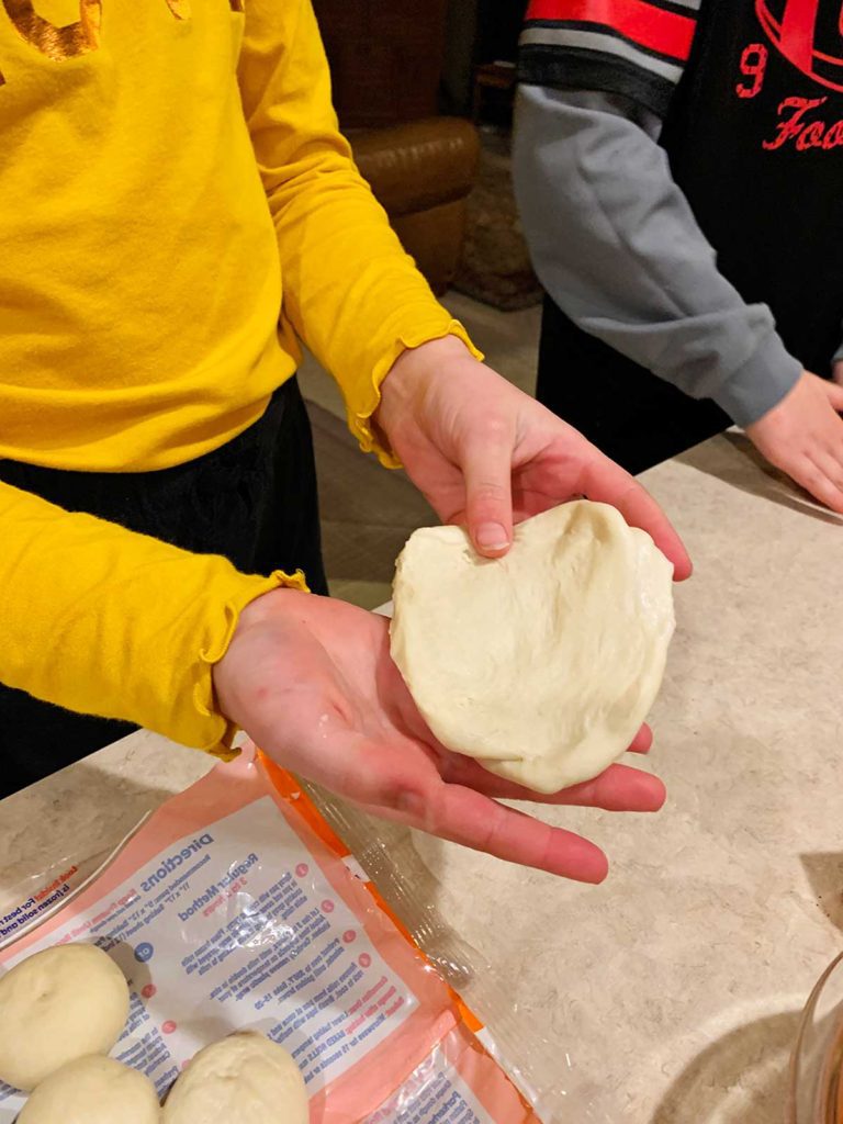 A child spreading a ball of dough into a flat circle.