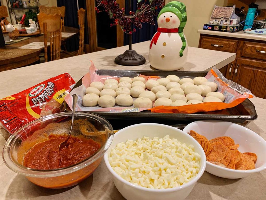 Marinara sauce, mozzarella cheese, pepperoni, and dough balls on a countertop.