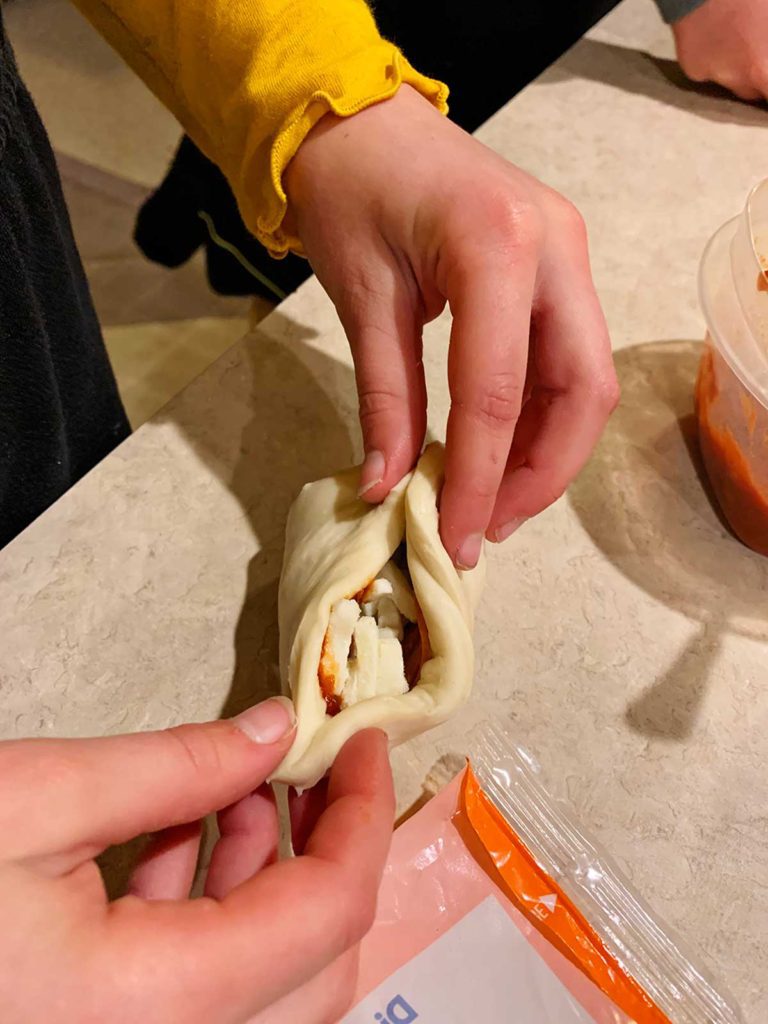 A child sealing marinara and cheese inside some dough.