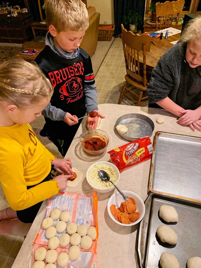 Children adding marinara, cheese and pepperoni to spread dough to make pizza pockets.