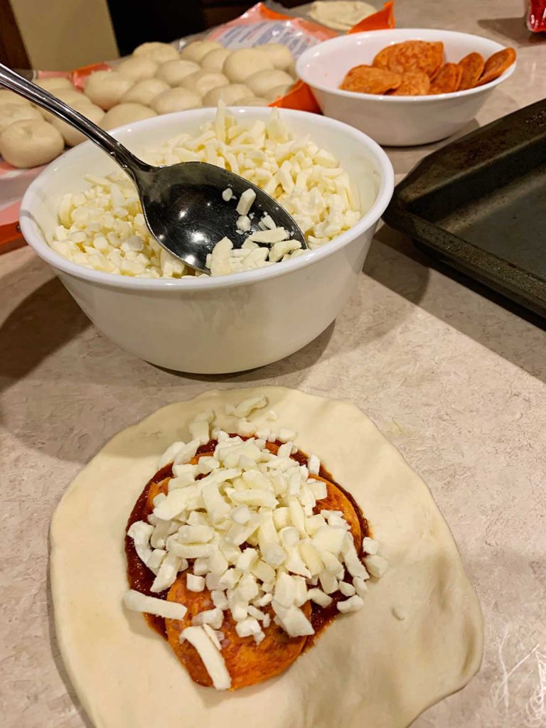 A spoon adding mozzarella to an open pizza pocket.