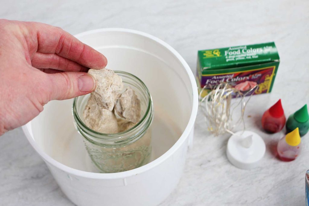 Adding rocks to a jar sitting inside an empty bucket