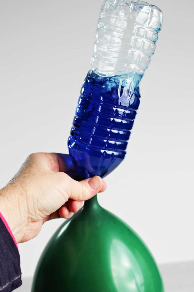 A bottle of blue water pouring into a balloon.