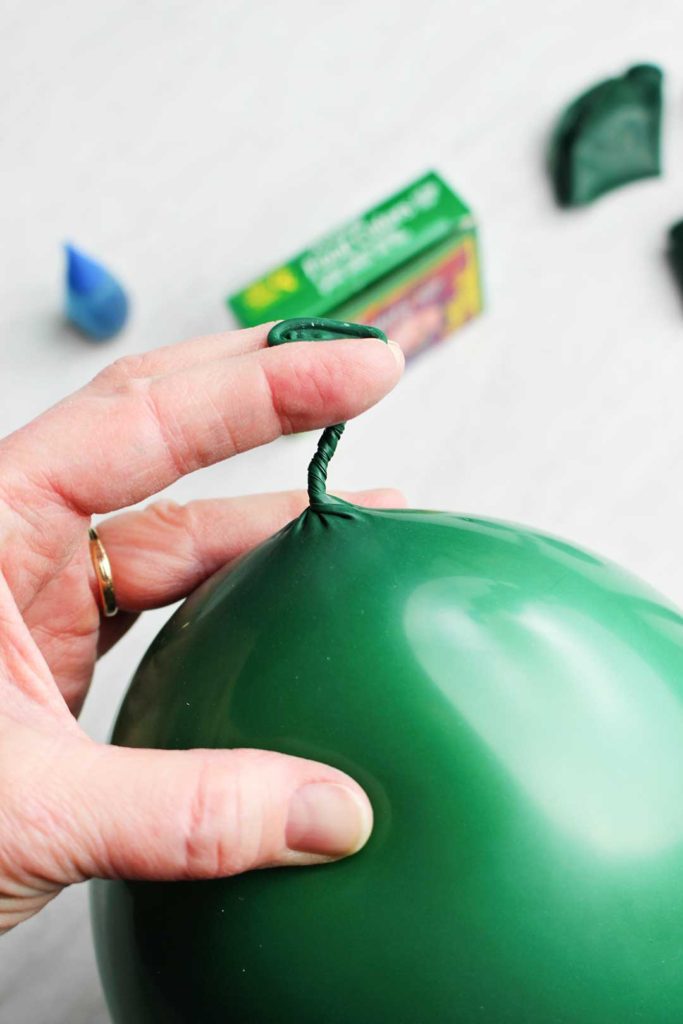 Twisting the end of a green balloon filled with air.