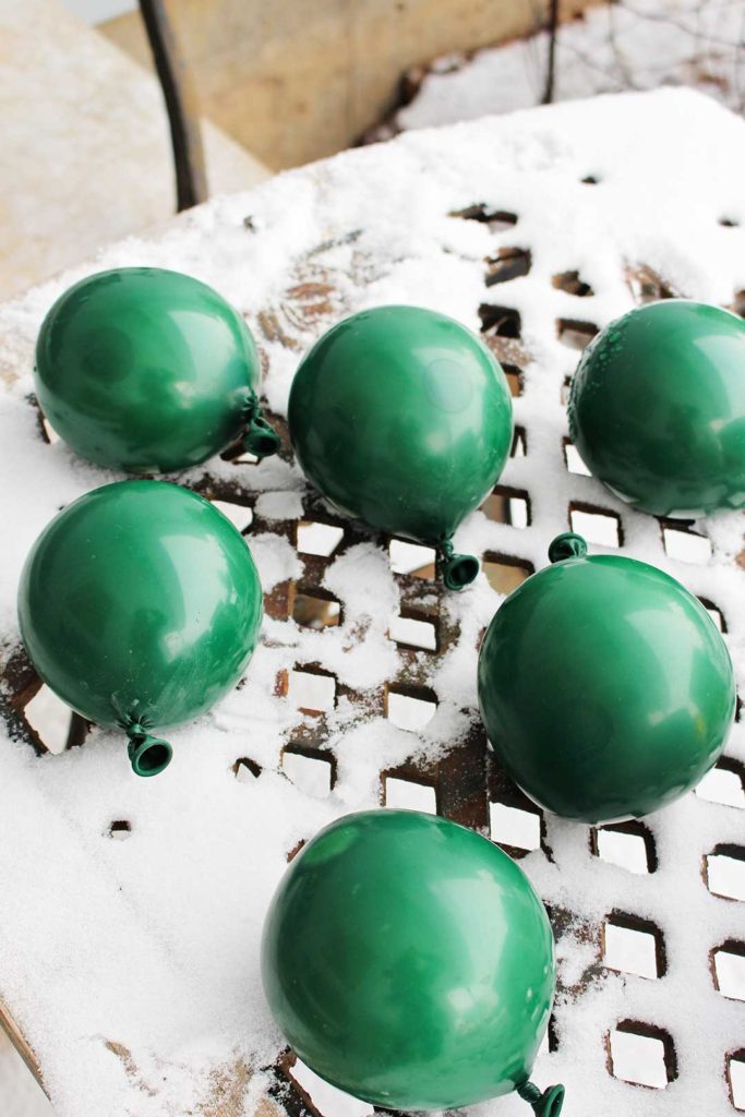 Green balloons filled with water sitting outside on a table with snow.