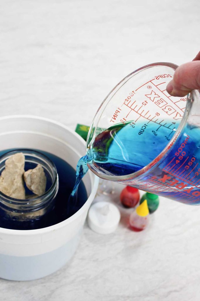Pouring water with blue food coloring into a bucket.