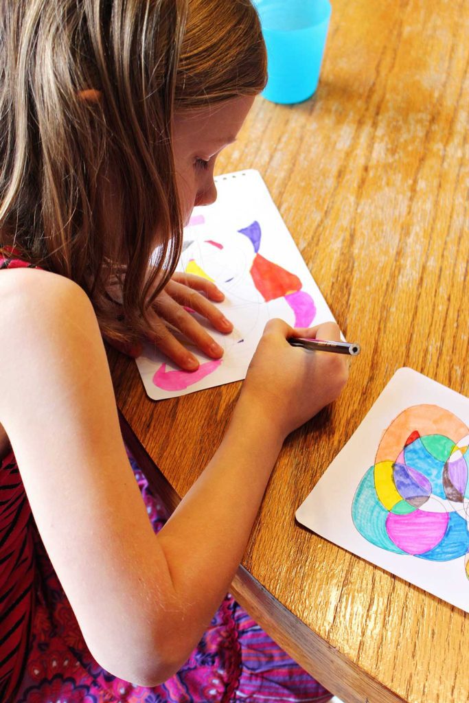 A child using a colored pencil to color shapes in her scribble art project.