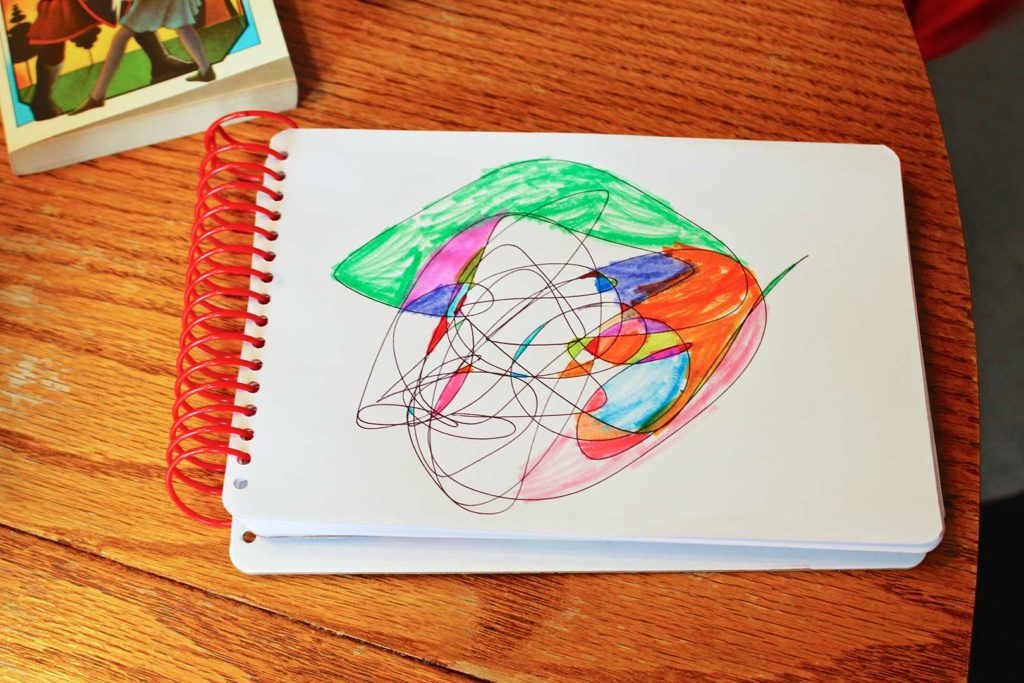 Colorful shapes of scribble art filled in with markers on a white notepad of paper.