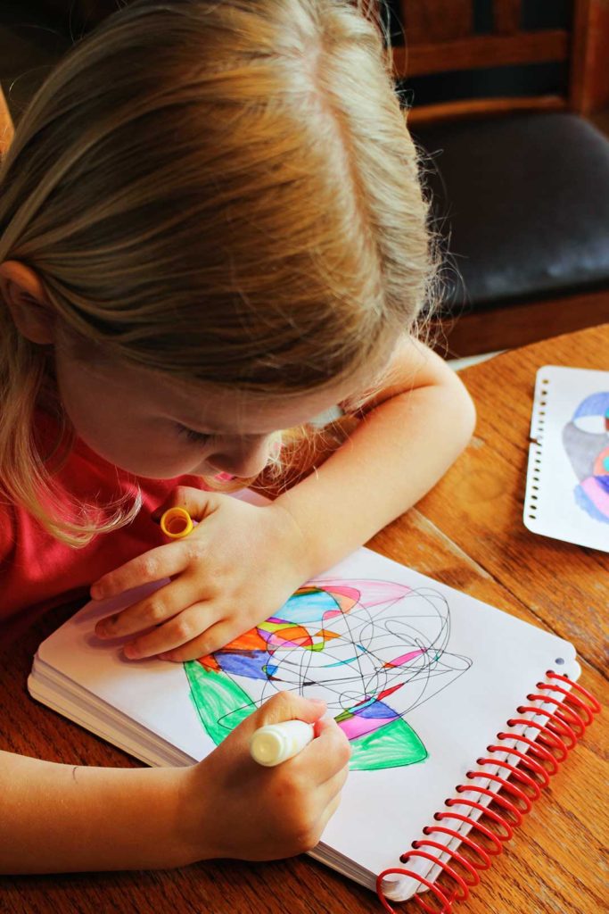 A child using a yellow marker to color in shapes on her notepad of paper.