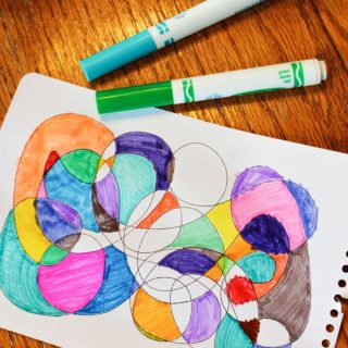 A child's scribble art project filled in with bright colors, surrounded by markers.