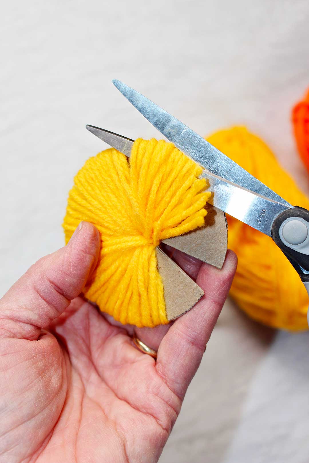 Scissors cutting the yellow yarn wrapped around a cardboard circular shape.