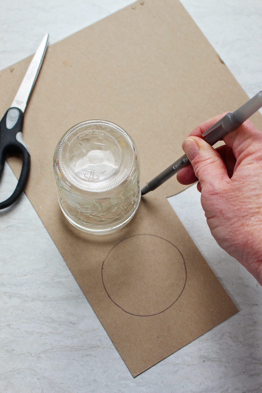 Using a jar to draw a circle on cardboard with a pen, a pair of scissors nearby.