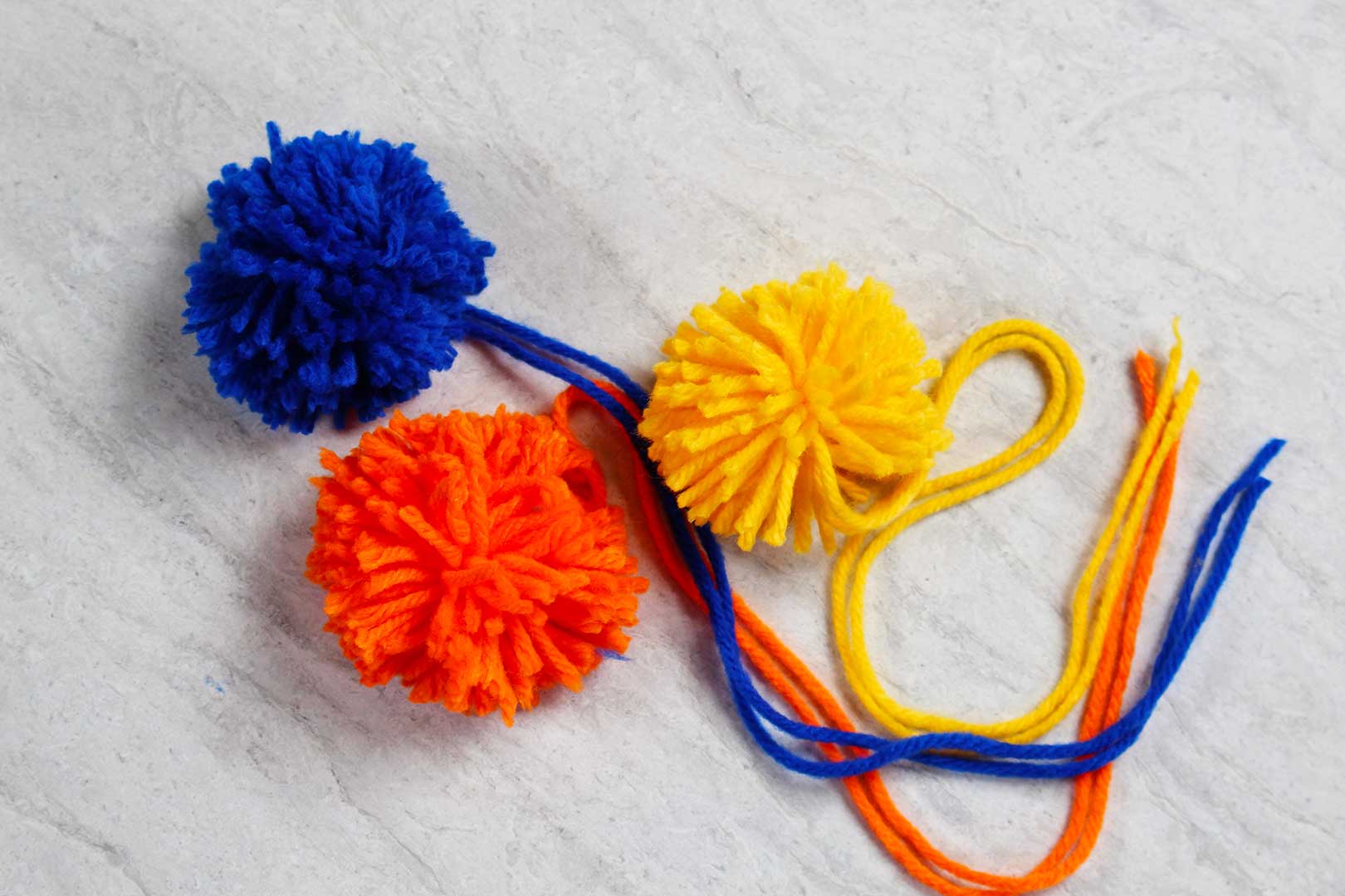 Blue, yellow and orange DIY pom pom bookmarks.