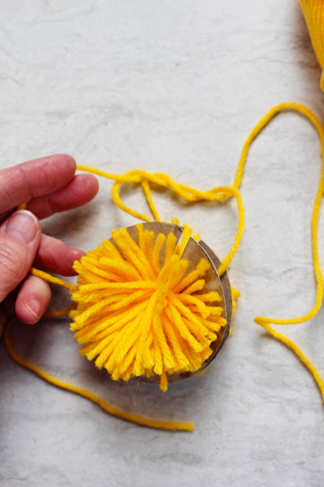 Yellow yarn cut into a pom pom shape.