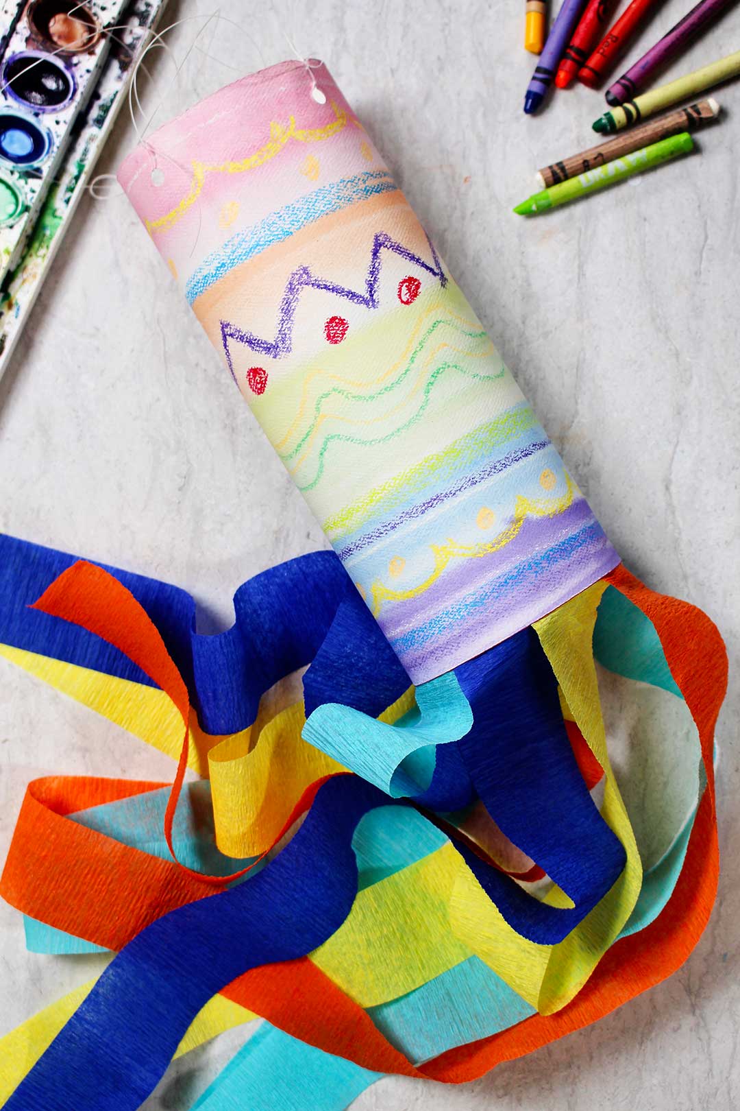 A brightly colored Watercolor Resist Painted Windsock for Kids with streamers.