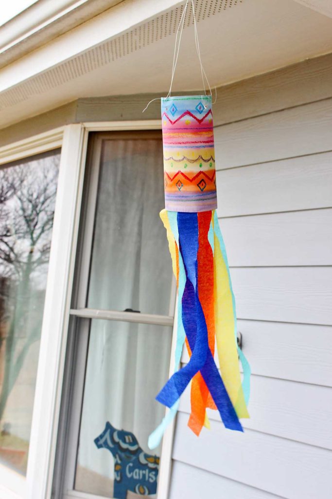 A brightly colored Watercolor Resist Painted Windsock for Kids with streamers, waving in the breeze..