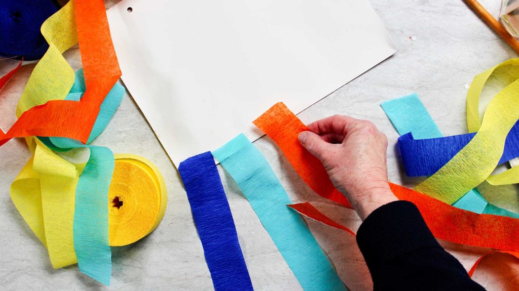 Orange, teal and blue streamers being attached to a piece of paper.