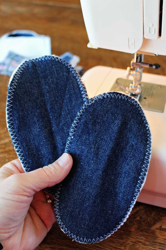 Denim fabric sewed together to make soft soles for baby shoes, a sewing machine in the background.