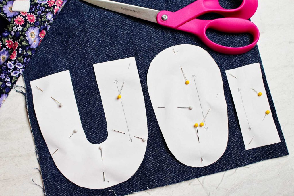 Pattern pieces pinned to blue denim fabric, fabric scissors nearby.