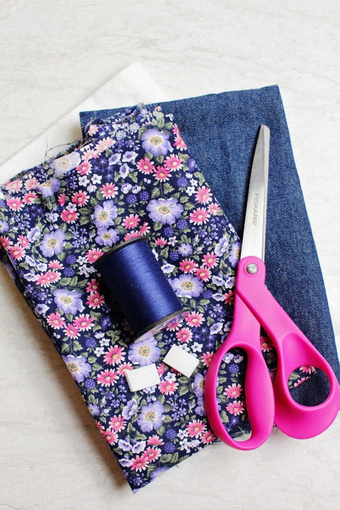 Pink and purple floral fabric, denim fabric, blue thread, velcro, and a pair of scissors.