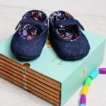 DIY Denim and floral soft soled baby shoes sitting on a set of baby books near a baby toy.