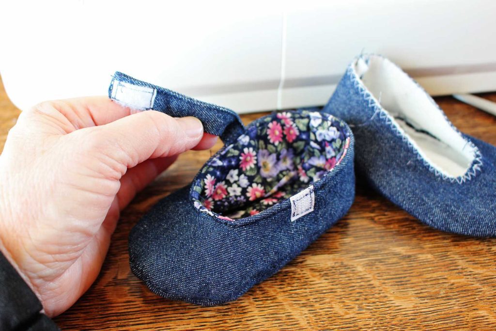 Securing a velcro strap on denim and floral homemade fabric baby shoes.