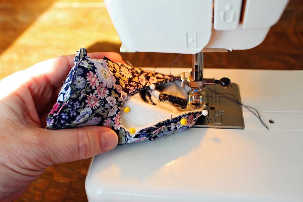 Sewing the lining on floral fabric baby shoes, held together by push pins.