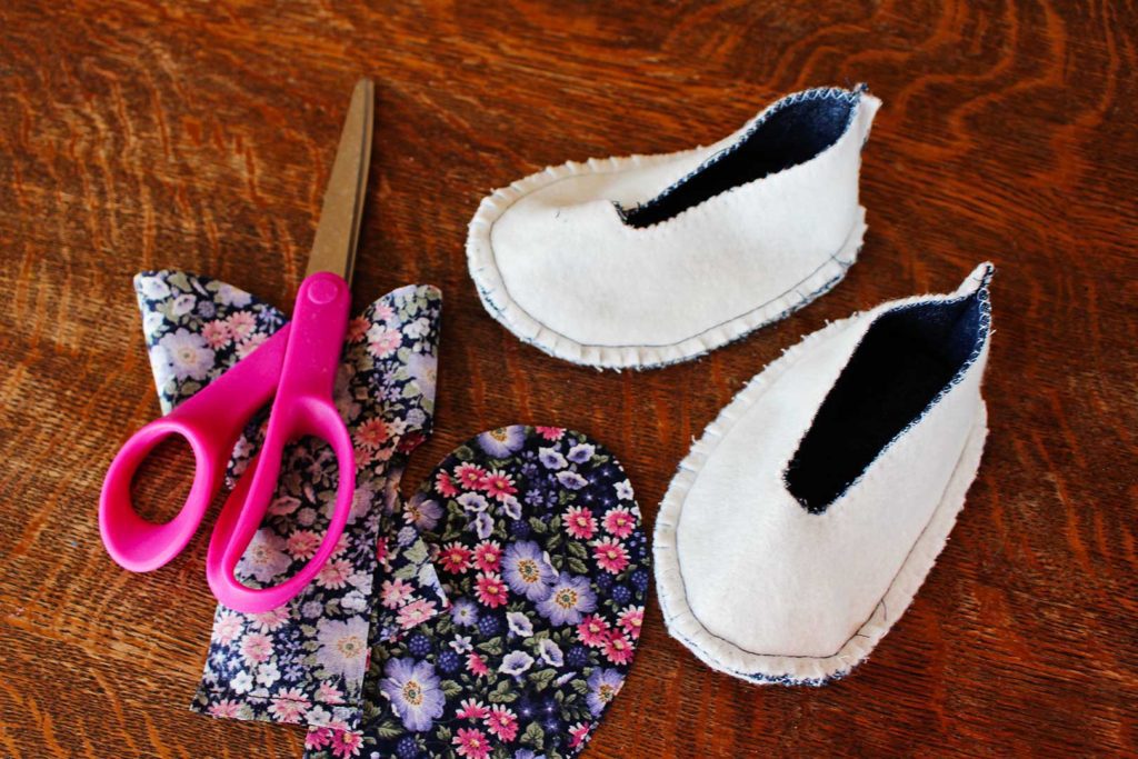 Floral fabric and a pair of scissors next to the outer lining of fabric baby shoes.
