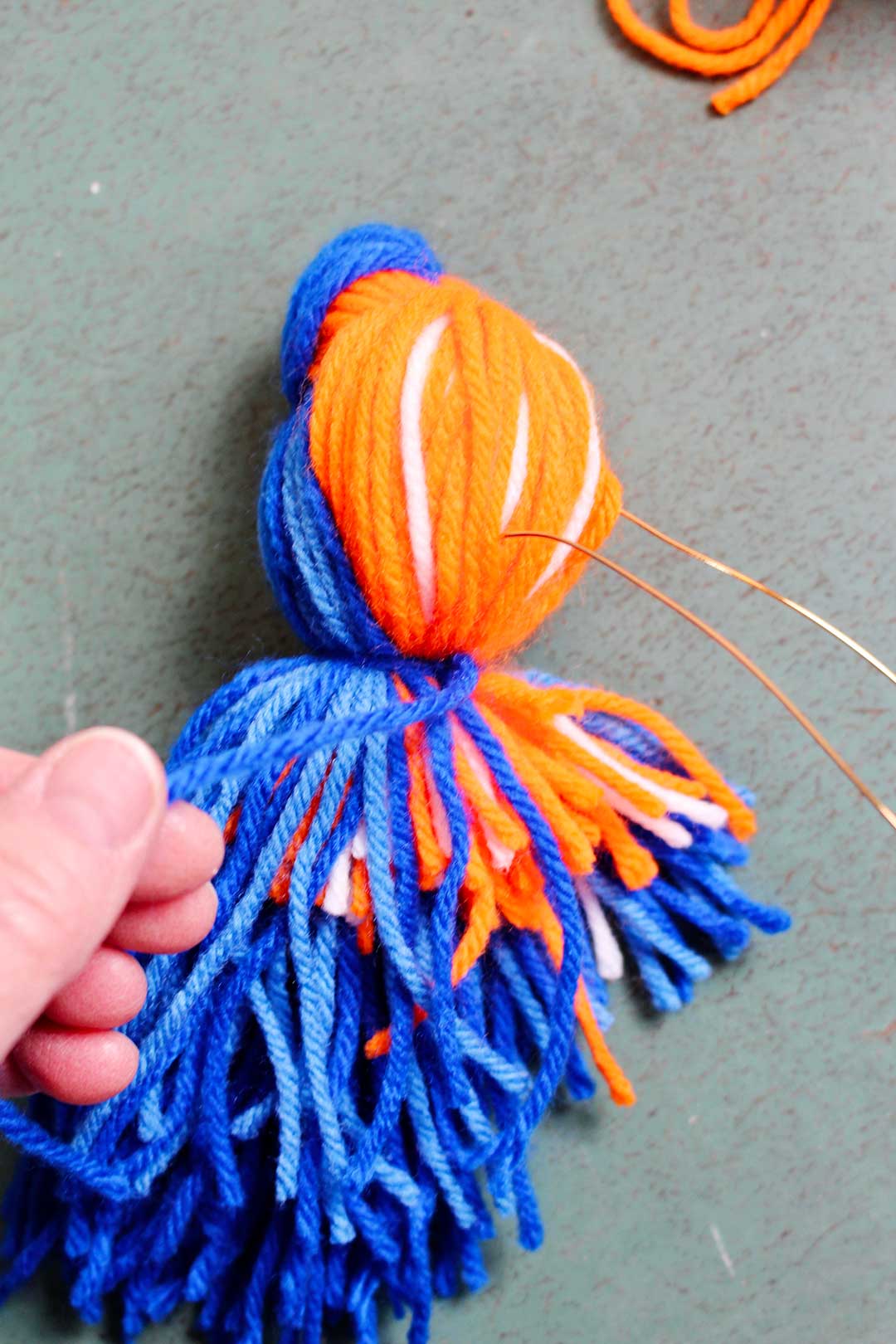 Tying a piece of blue yarn around the "tail" of a yarn bird.