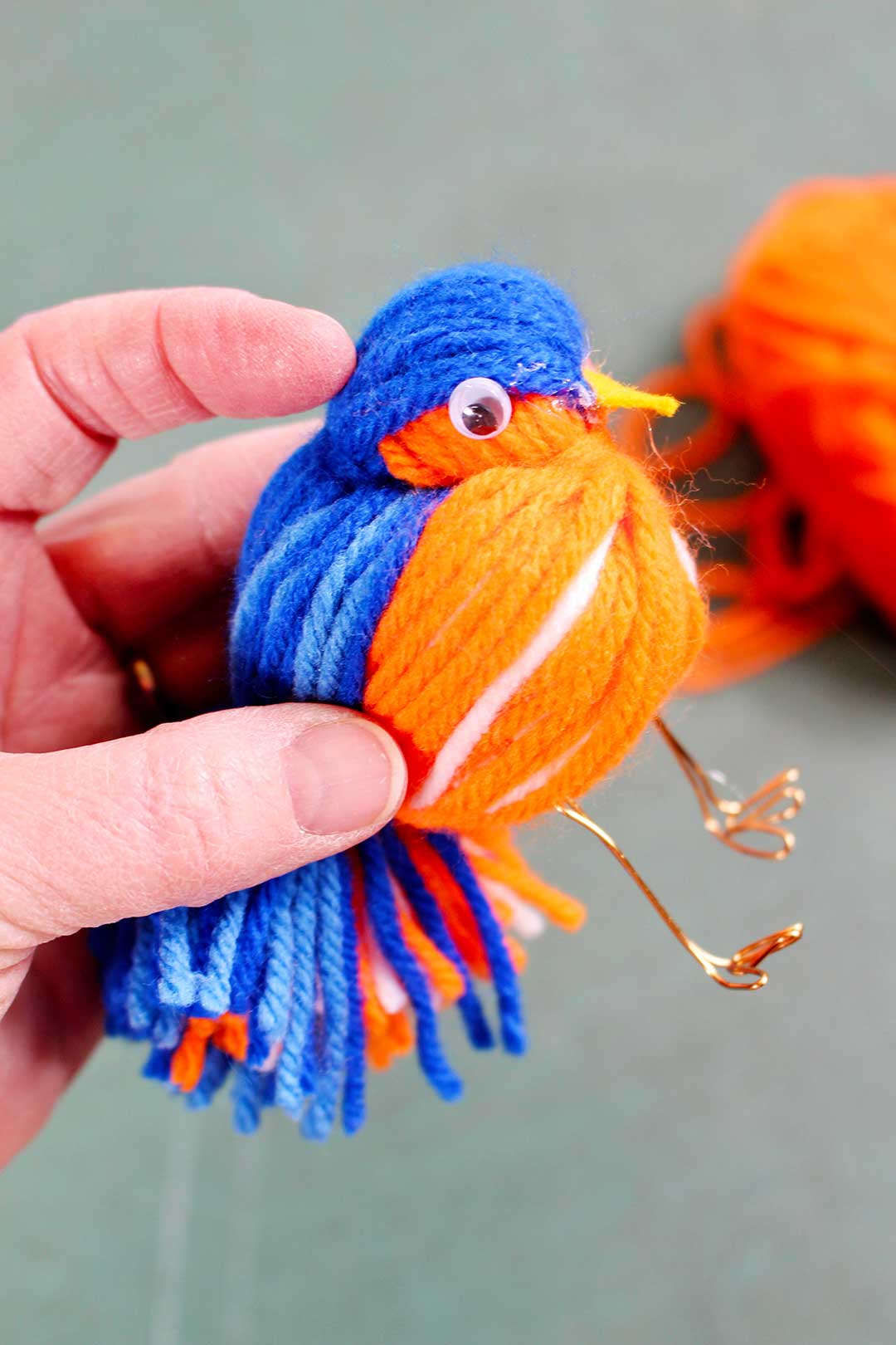 A googly eye hot glued to the head of a yarn bird.