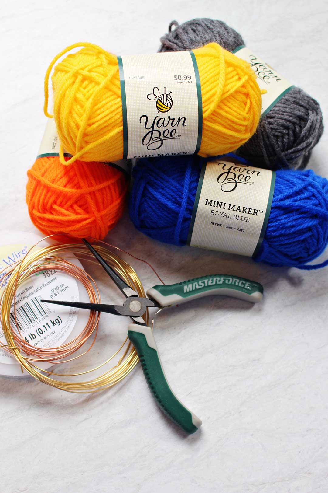 Skeins of yellow, blue, orange, and grey yarn near wire and a pair of needle nose pliers.