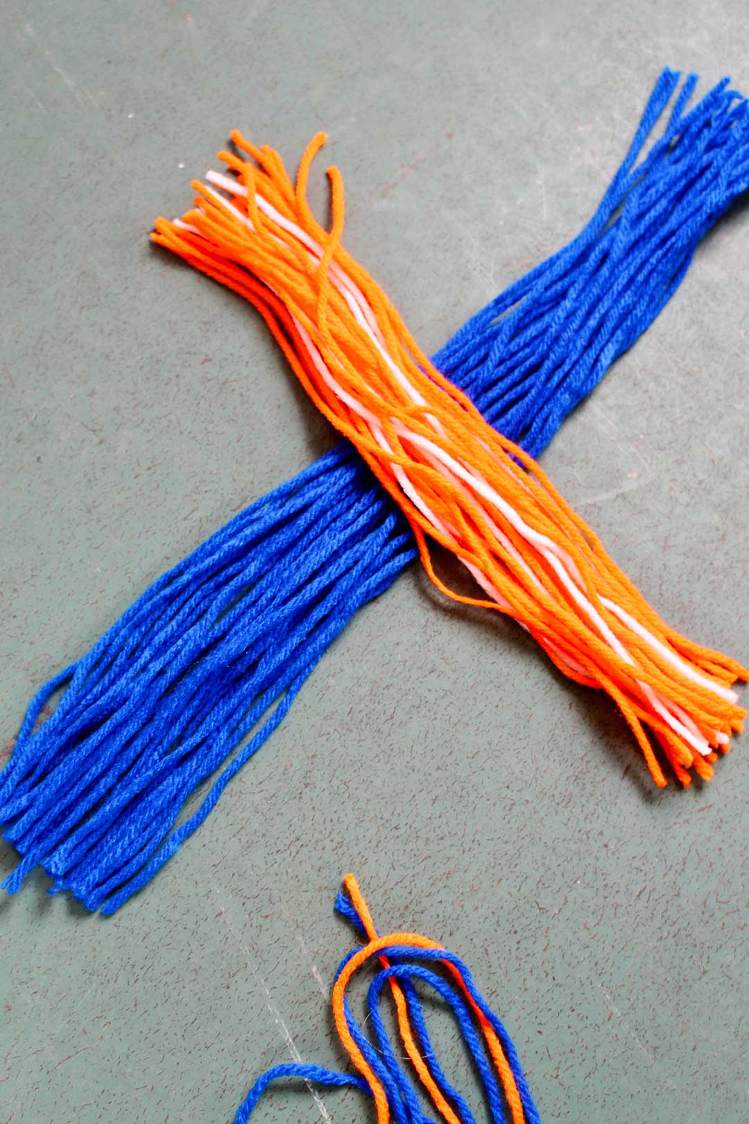 Strands of blue yarn in a bunch lying crosswise with strands of orange and white yarn in a bunch.