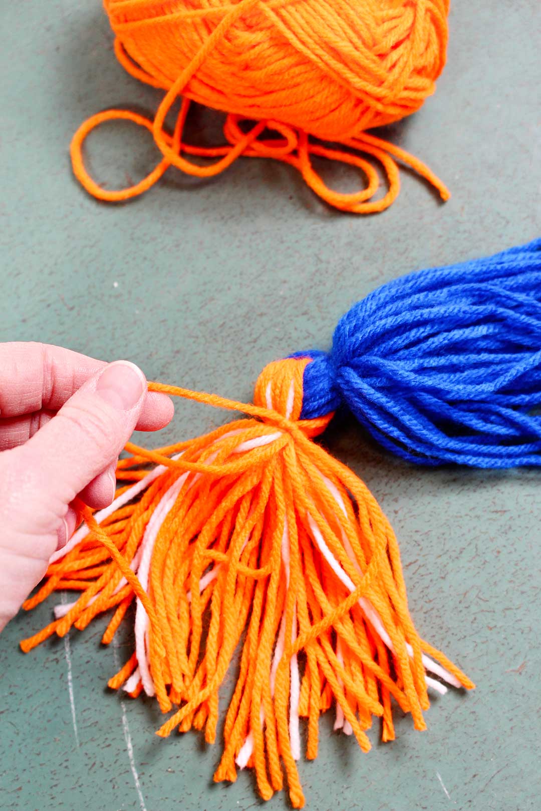 Wrapping a piece of orange yarn around a bunch of yarn.