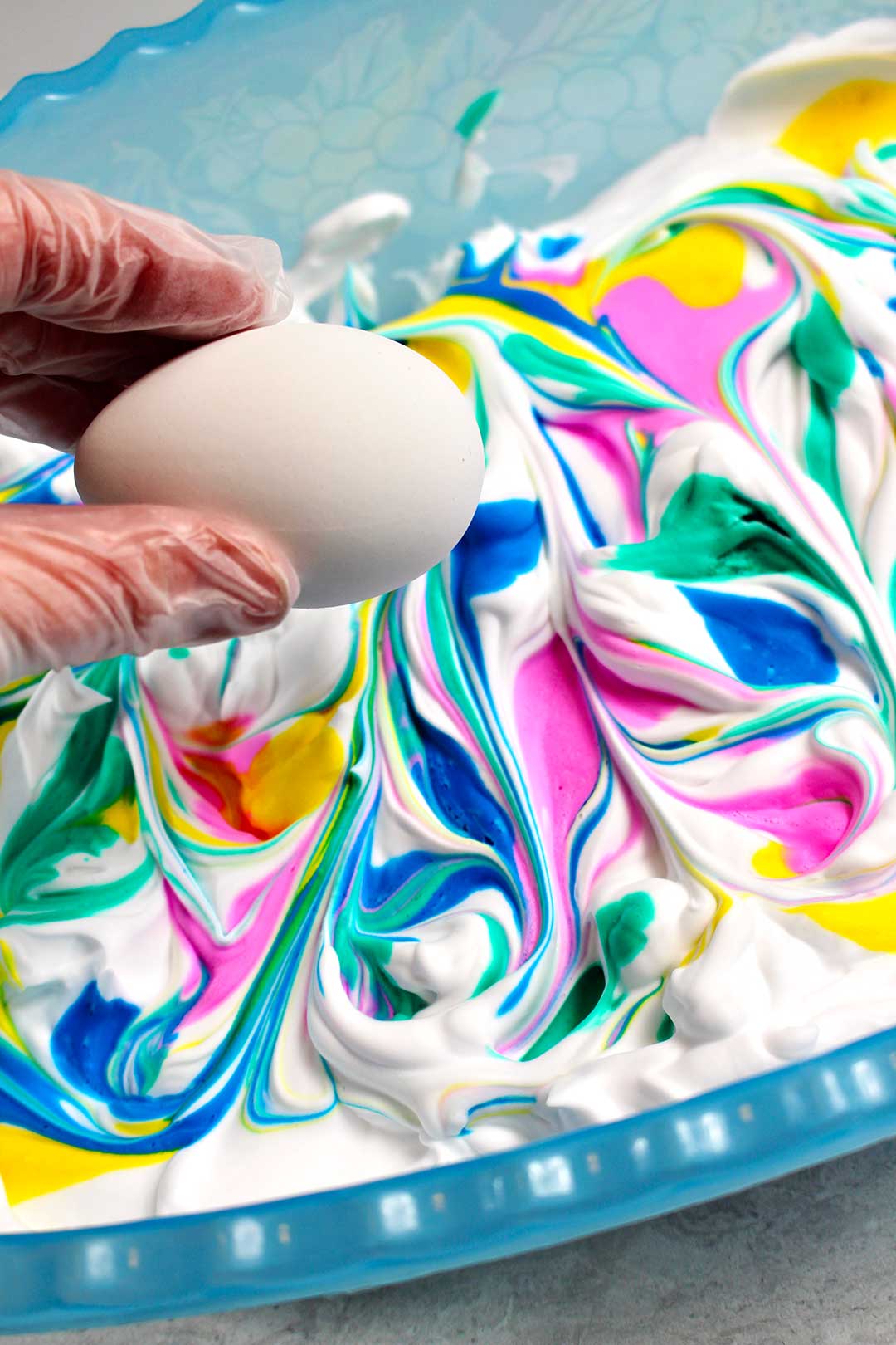 Dipping an egg into a yellow, green, pink, and blue swirled shaving cream.