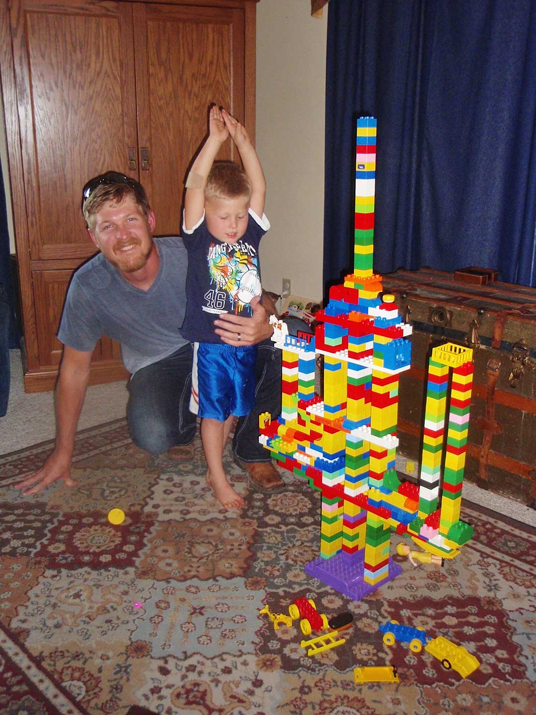 A child and his father building a tower of LEGO bricks.