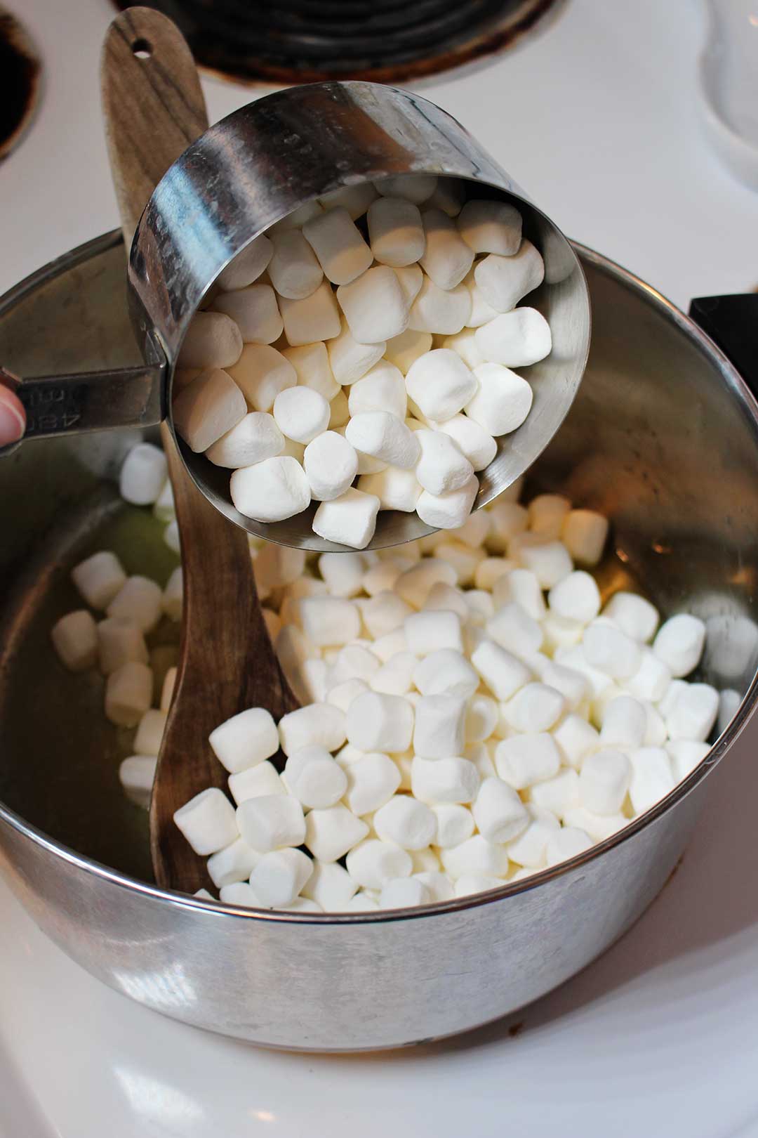 Pouring marshmallows into a pan on the stove from a measuring cup.