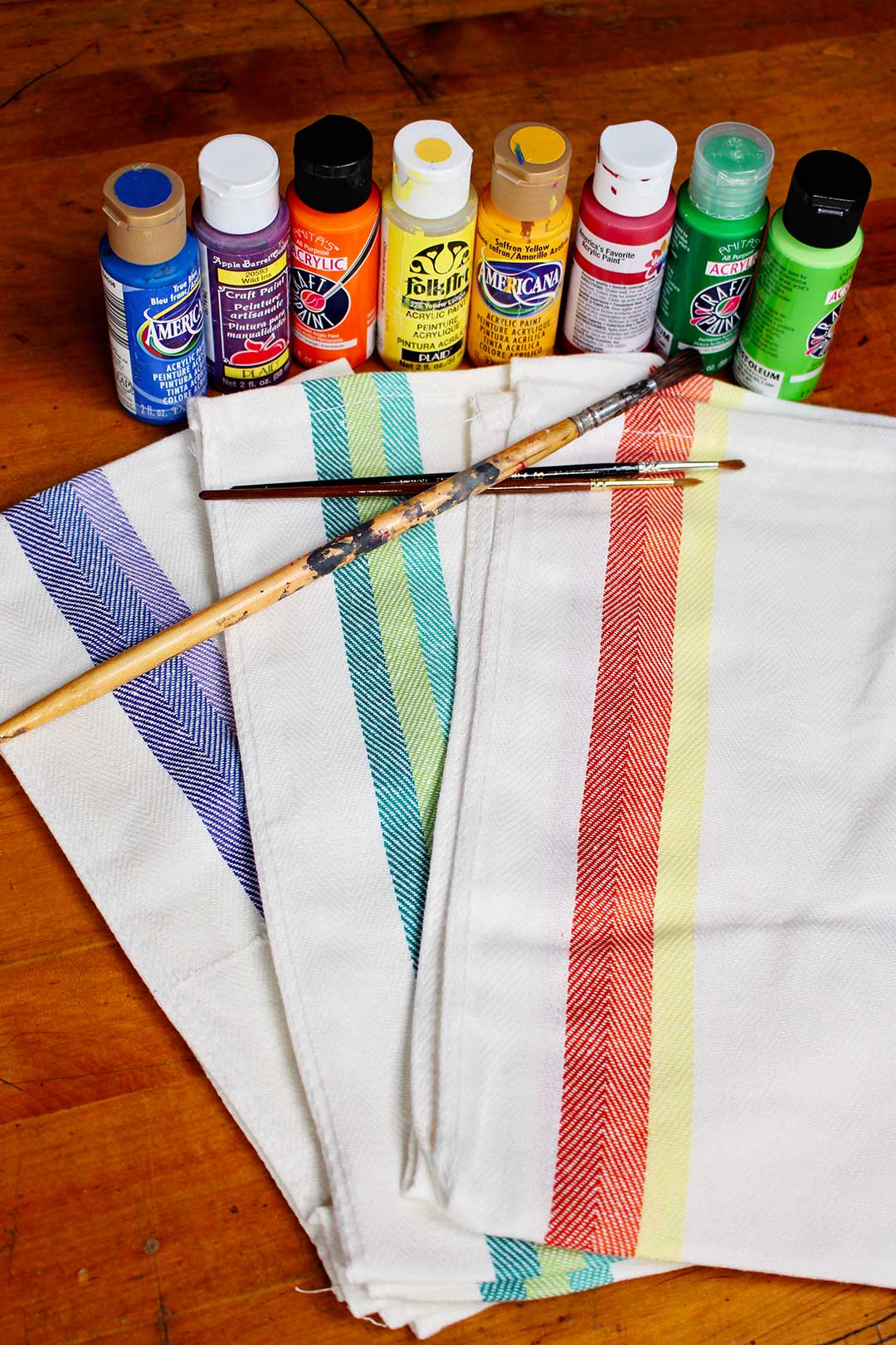 Colorful dish towels, paint brushes, and a rainbow of paint bottles.
