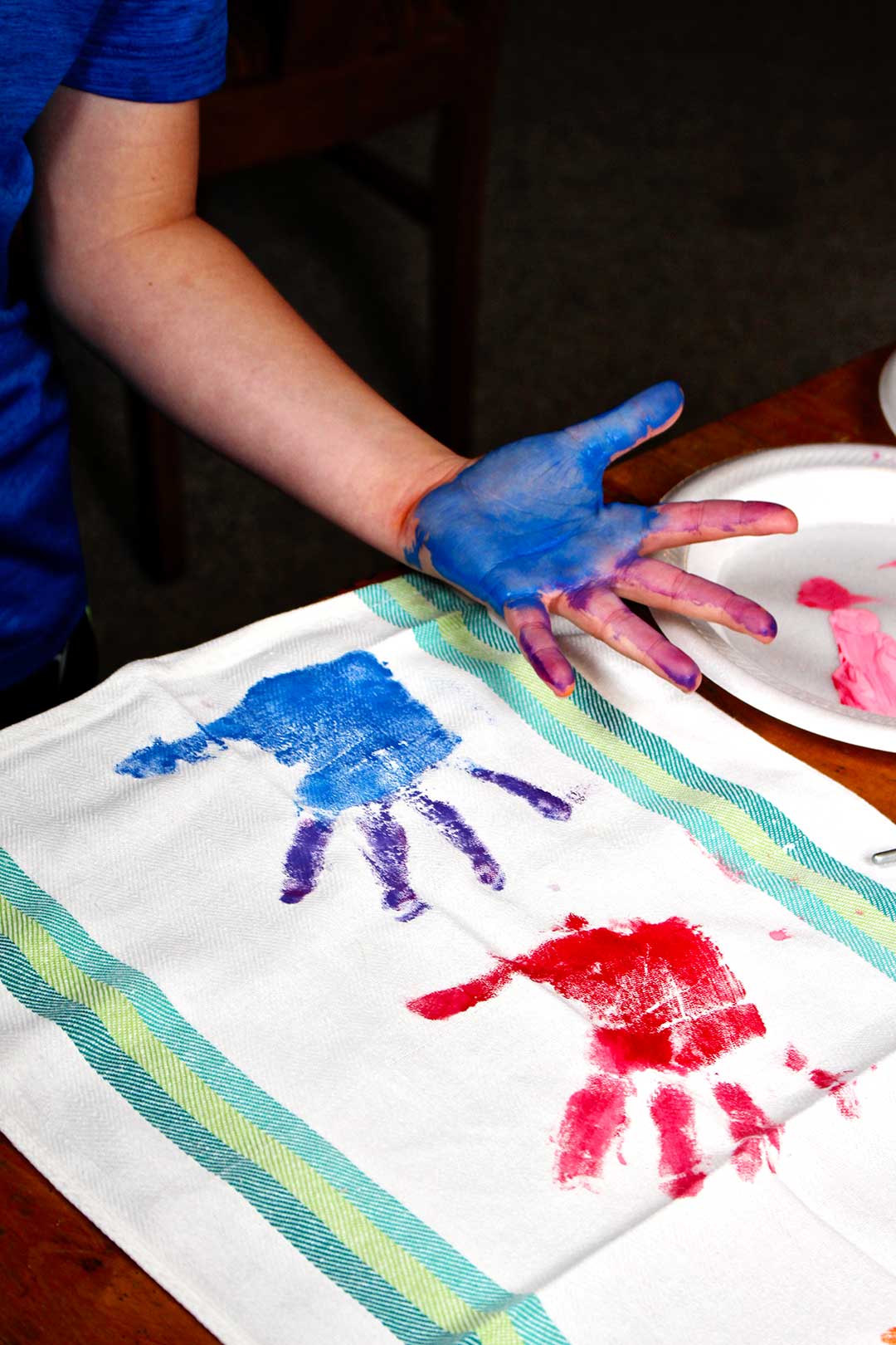 A child's hand painted blue and red and purple, leaving a handprint on a dish towel.