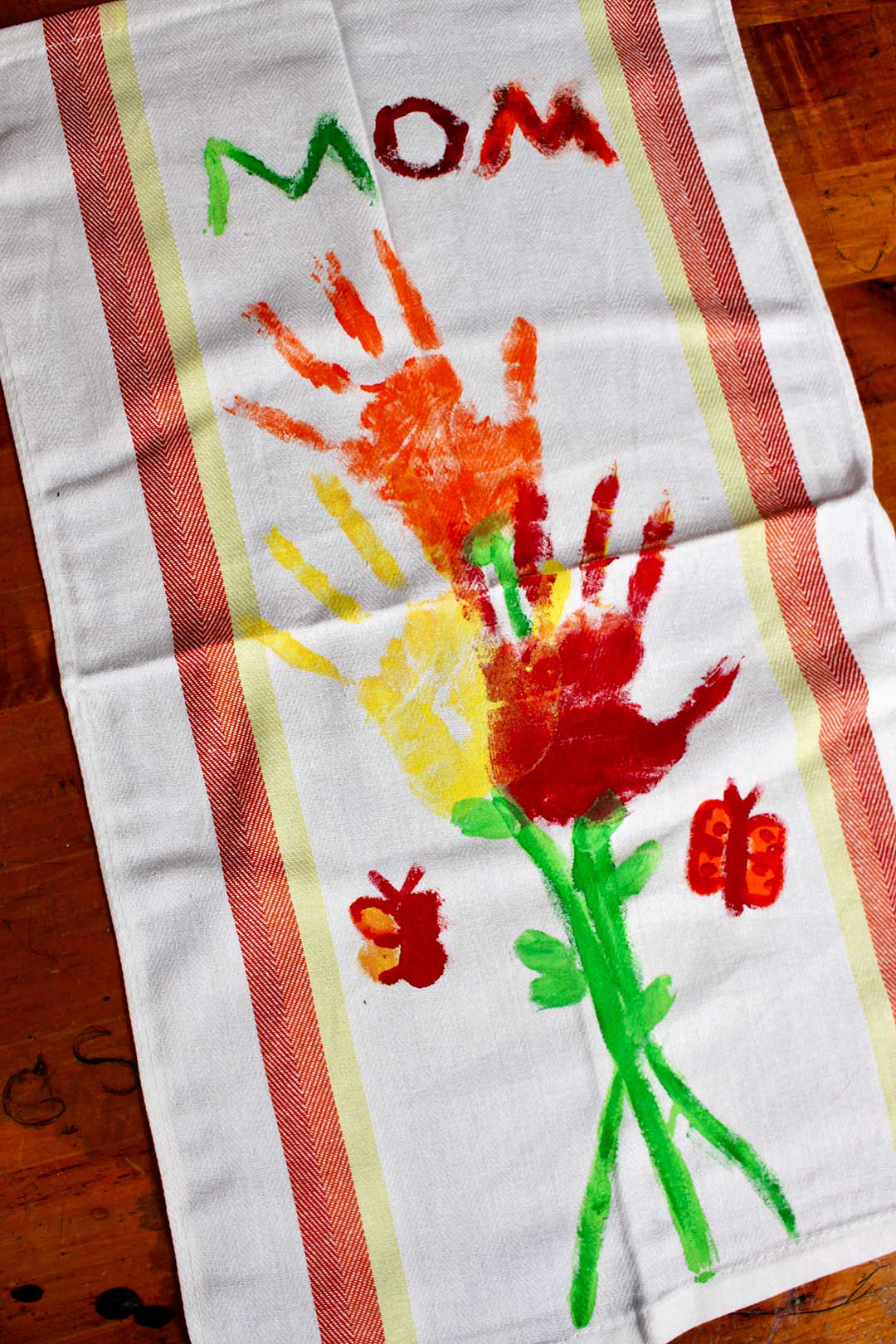 A dish towel with colorful painted handprint flowers and the word, "Mom".