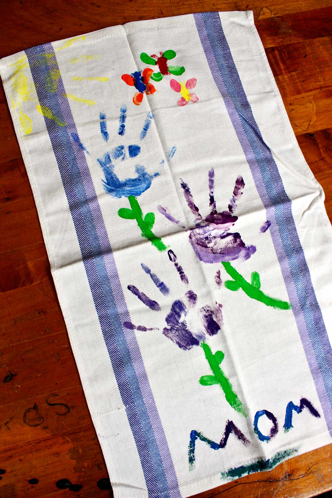 A dish towel with colorful painted handprint flowers and the word, "Mom".