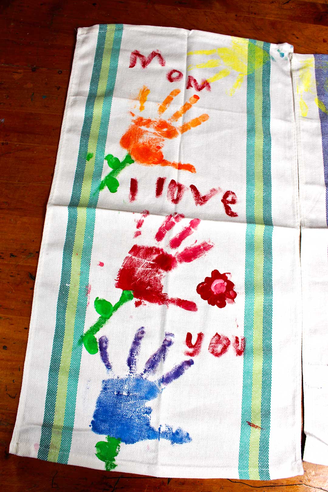 A dish towel with colorful painted handprint flowers and the words, "Mom I love you".