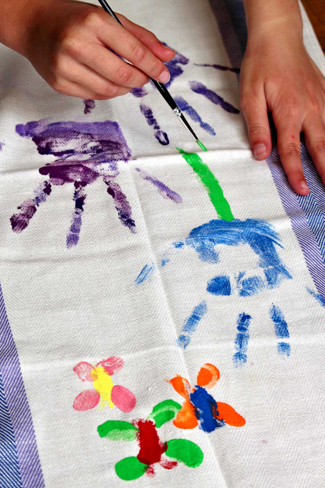 A child painting a green stem on a blue handprint to create a flower on fabric..