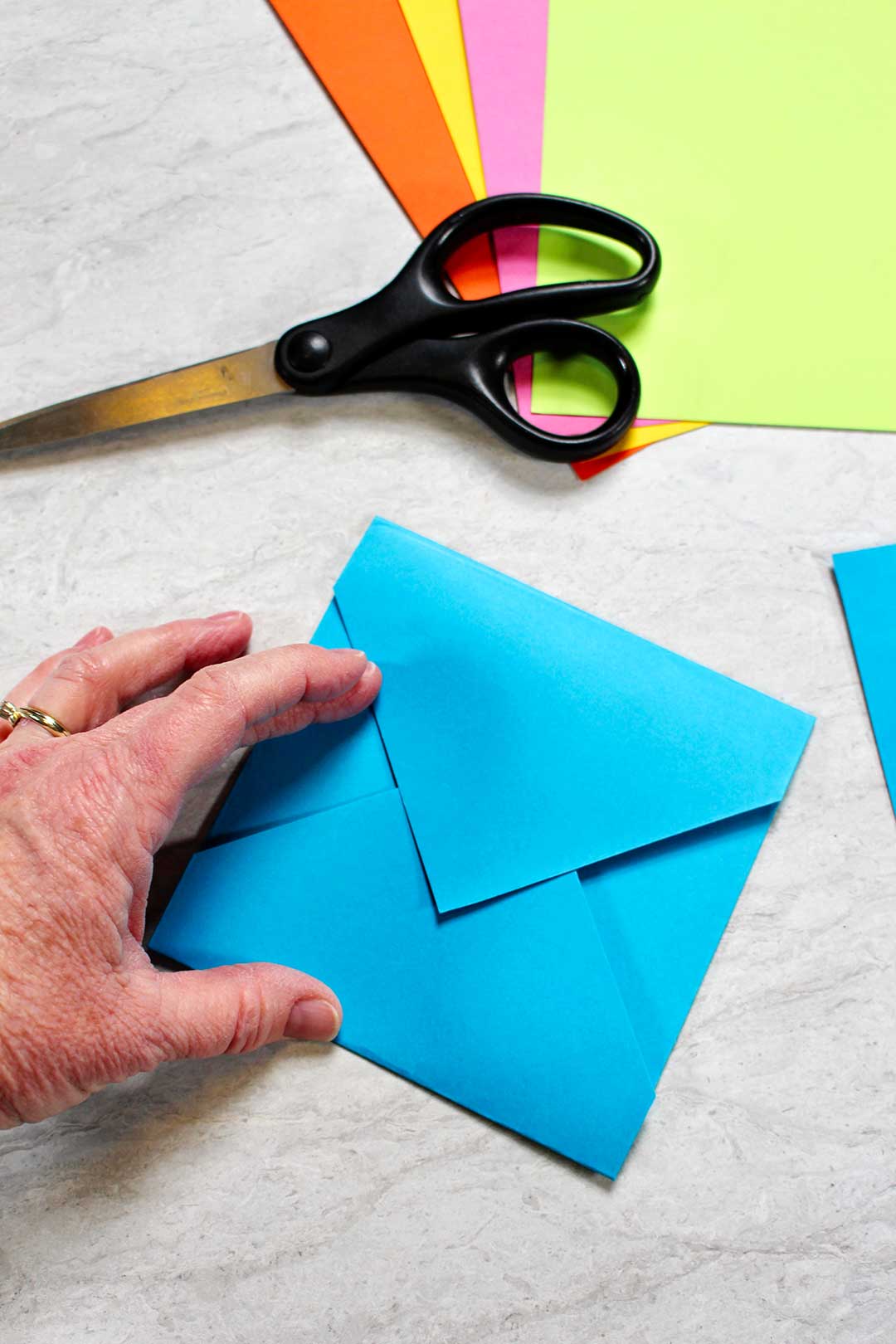 A homemade blue envelope near a pile of colorful paper and a pair of scissors.